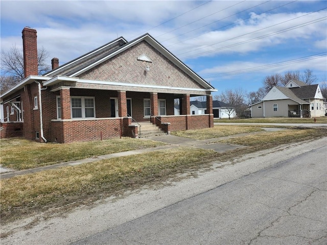 view of front facade featuring covered porch, brick siding, a chimney, and a front lawn