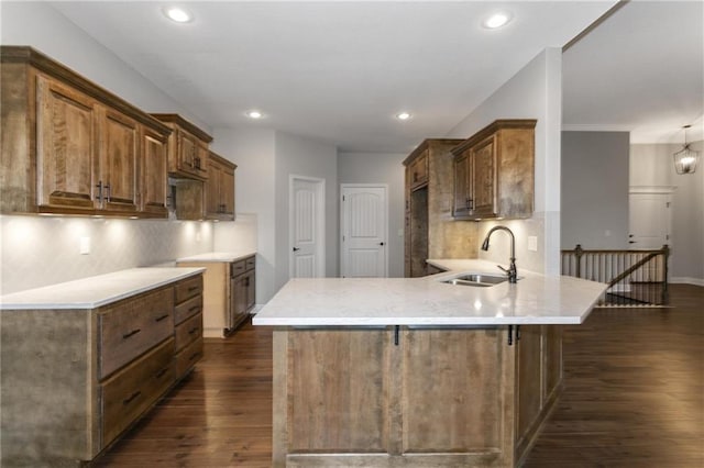 kitchen with dark wood-style floors, a peninsula, backsplash, and a sink