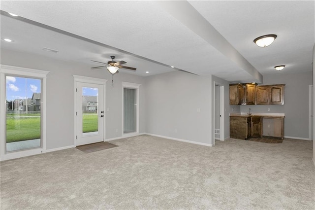 unfurnished living room featuring ceiling fan, baseboards, a textured ceiling, and light colored carpet