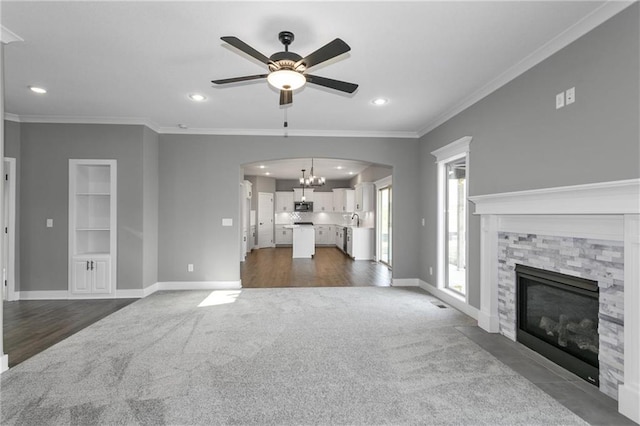 unfurnished living room with a stone fireplace, built in features, baseboards, ornamental molding, and dark carpet