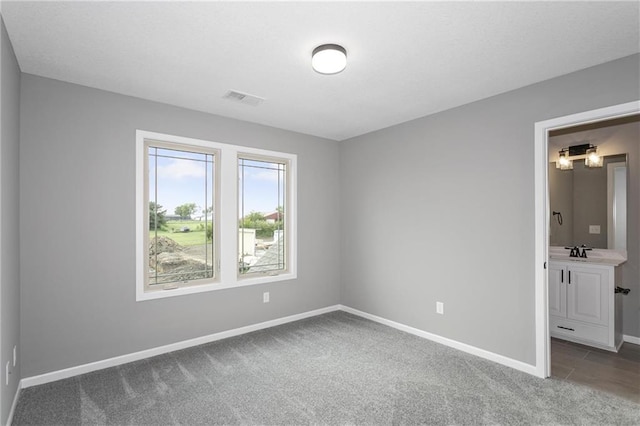 unfurnished bedroom featuring baseboards, visible vents, dark colored carpet, and a sink