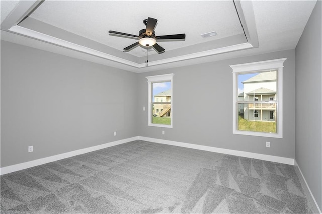 carpeted spare room with a ceiling fan, a raised ceiling, visible vents, and baseboards