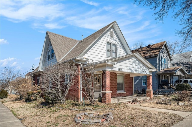 view of front of home with covered porch, roof with shingles, and brick siding