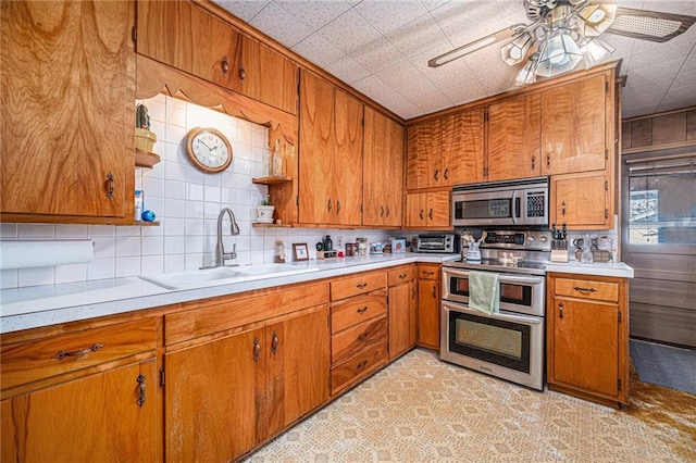 kitchen featuring stainless steel appliances, brown cabinetry, a sink, and light countertops