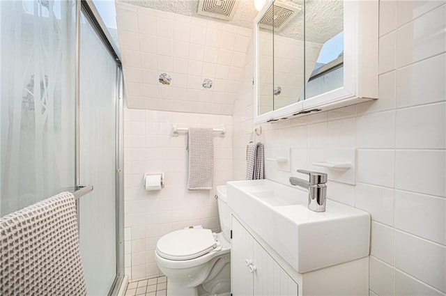 bathroom featuring tile walls, toilet, a stall shower, vanity, and tile patterned floors