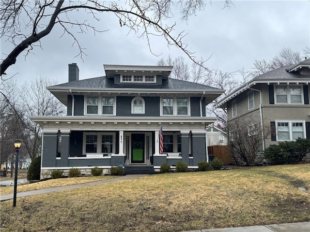 american foursquare style home with a porch, a chimney, a front lawn, and roof with shingles