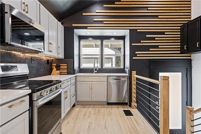 kitchen with lofted ceiling, a sink, light wood-style floors, appliances with stainless steel finishes, and decorative backsplash