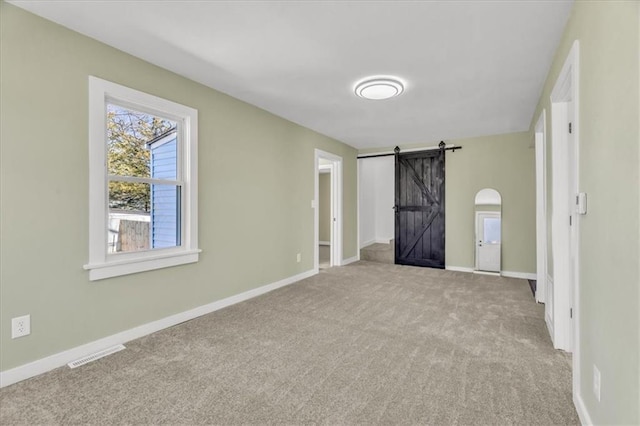 spare room featuring a barn door, baseboards, visible vents, and carpet flooring