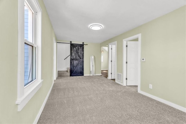 carpeted empty room with a barn door, baseboards, visible vents, and a wealth of natural light