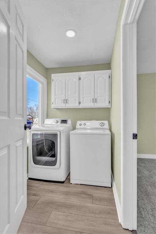 washroom with light wood-type flooring, cabinet space, baseboards, and washer and clothes dryer