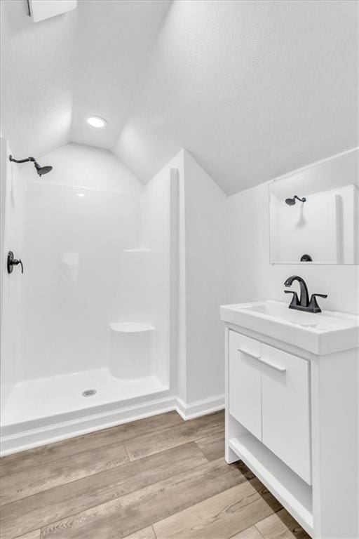 bathroom featuring lofted ceiling, wood finished floors, baseboards, walk in shower, and vanity