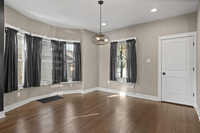 empty room featuring a notable chandelier, visible vents, a healthy amount of sunlight, and wood finished floors