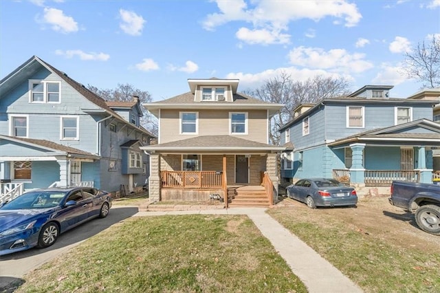 american foursquare style home with roof with shingles, covered porch, and a front yard