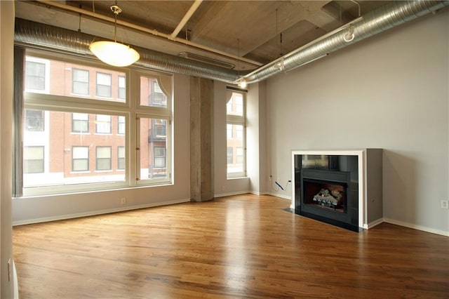 unfurnished living room with a fireplace with flush hearth, wood finished floors, and baseboards