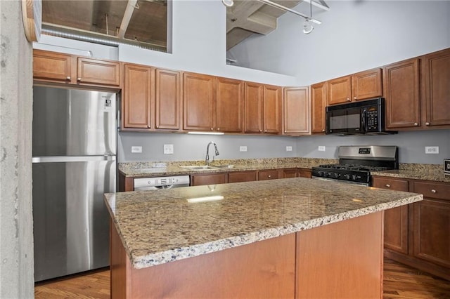 kitchen featuring light stone counters, appliances with stainless steel finishes, a towering ceiling, wood finished floors, and a sink