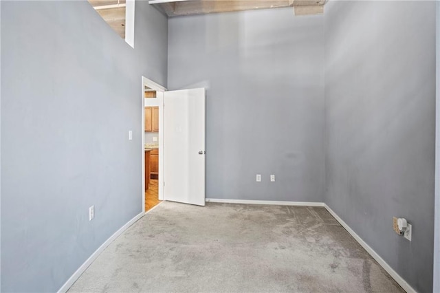 unfurnished room with baseboards, carpet, and a towering ceiling