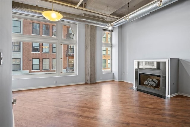 unfurnished living room featuring a fireplace with flush hearth, wood finished floors, and baseboards