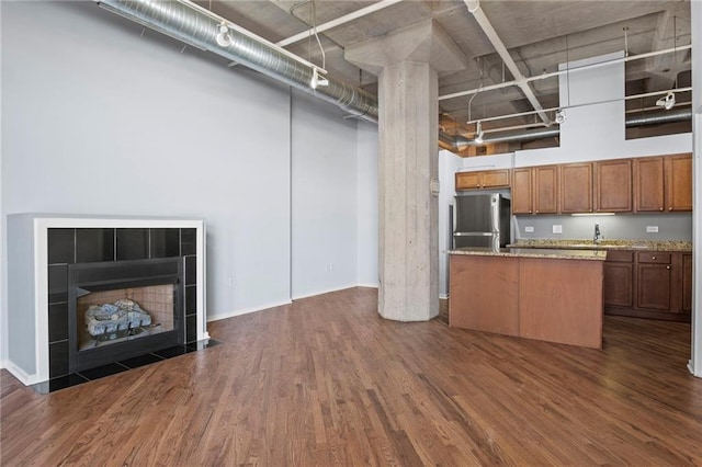 kitchen featuring dark wood finished floors, freestanding refrigerator, brown cabinetry, a fireplace, and a towering ceiling