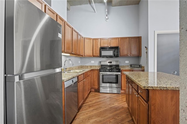 kitchen featuring light wood-type flooring, brown cabinets, a towering ceiling, stainless steel appliances, and a sink