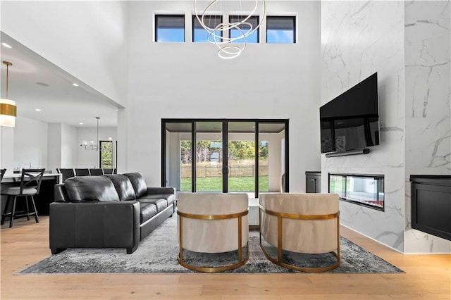 living area with a chandelier, recessed lighting, a premium fireplace, wood finished floors, and a towering ceiling