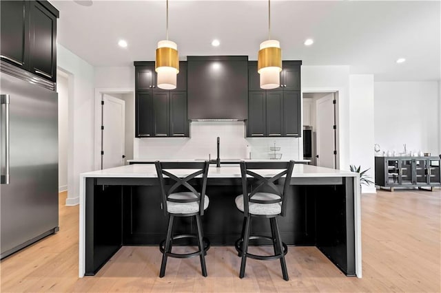 kitchen featuring light countertops, backsplash, light wood-style floors, stainless steel built in fridge, and premium range hood