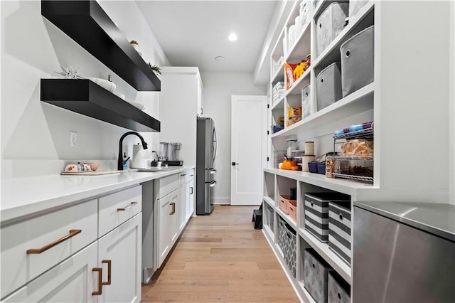 kitchen featuring light wood finished floors, open shelves, freestanding refrigerator, white cabinets, and a sink