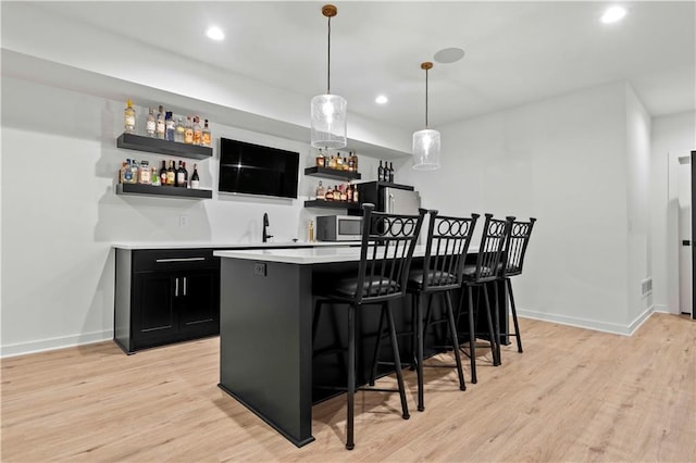 bar with recessed lighting, baseboards, light wood-style floors, stainless steel microwave, and indoor wet bar