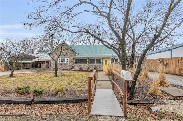 view of front facade featuring metal roof, stone siding, a carport, and fence