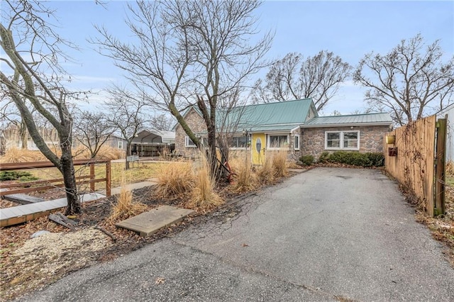 single story home featuring stone siding, fence, and metal roof