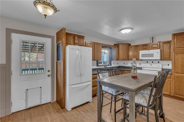 kitchen featuring dark countertops, white appliances, light wood finished floors, and brown cabinetry