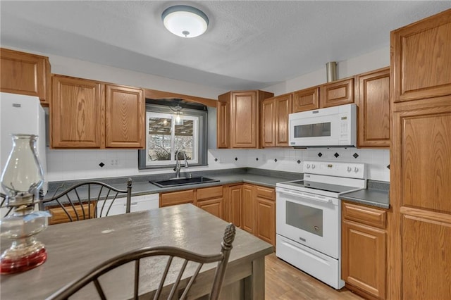 kitchen featuring tasteful backsplash, dark countertops, white appliances, and a sink