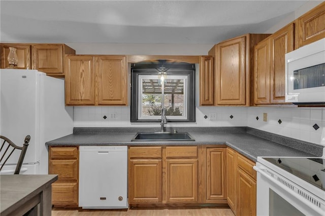 kitchen featuring brown cabinets, dark countertops, decorative backsplash, a sink, and white appliances