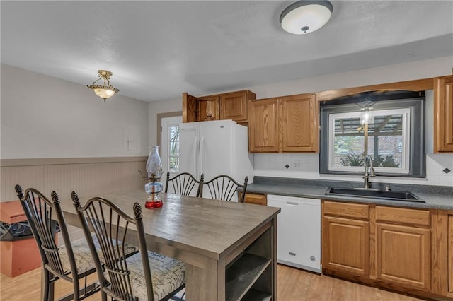 kitchen with white appliances, light wood finished floors, wainscoting, dark countertops, and a sink