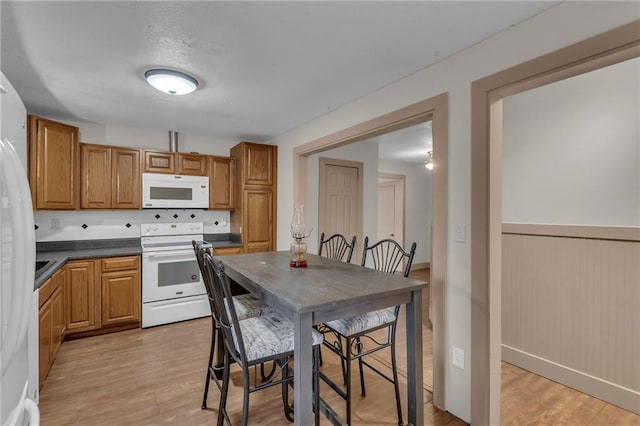 kitchen with white appliances, wainscoting, dark countertops, brown cabinets, and light wood-style floors