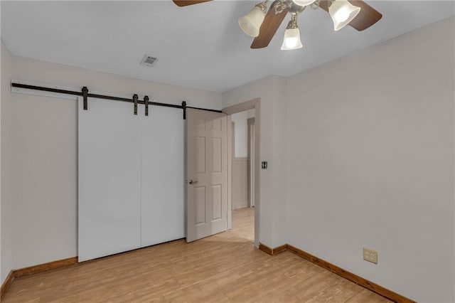 unfurnished bedroom featuring a barn door, baseboards, visible vents, a ceiling fan, and light wood-style floors