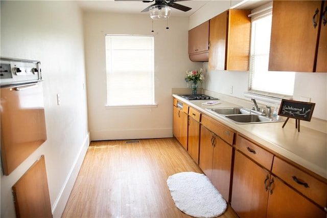 kitchen featuring light countertops, a sink, baseboards, brown cabinetry, and ceiling fan