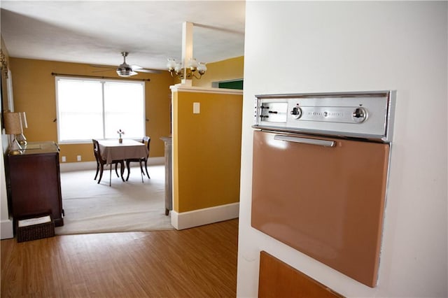 kitchen featuring baseboards, oven, wood finished floors, and ceiling fan with notable chandelier