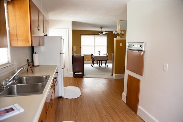 kitchen with brown cabinets, light wood finished floors, light countertops, a sink, and ceiling fan