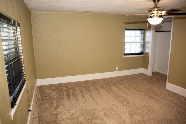 carpeted spare room featuring a textured wall, baseboards, and ceiling fan