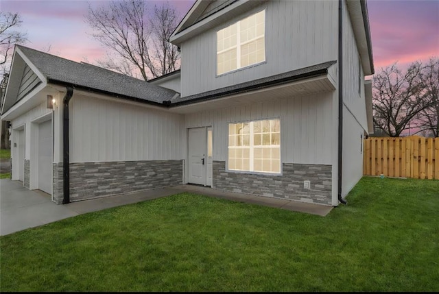 view of front of property with a front lawn, an attached garage, fence, and stone siding