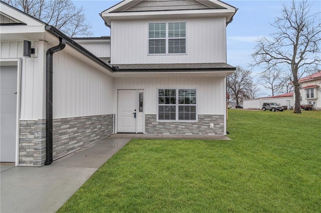 entrance to property with a yard, stone siding, and an attached garage