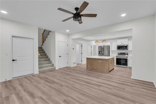 kitchen featuring light wood finished floors, a kitchen island, open floor plan, stainless steel appliances, and white cabinetry