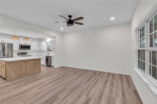 kitchen with light wood-type flooring, a sink, a kitchen island, appliances with stainless steel finishes, and light countertops