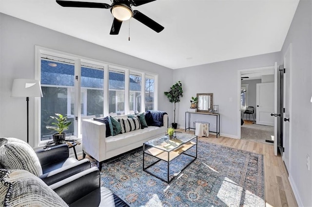 living room featuring baseboards, light wood-style flooring, and a ceiling fan