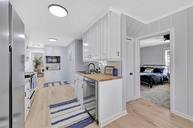 kitchen featuring light wood finished floors, a sink, white cabinets, appliances with stainless steel finishes, and butcher block counters