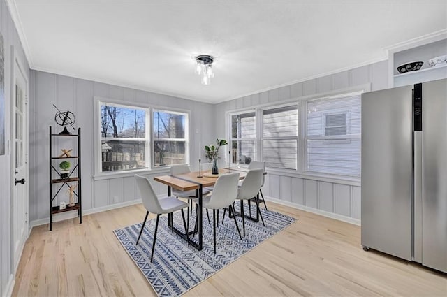 dining area featuring light wood-style floors, crown molding, and a decorative wall