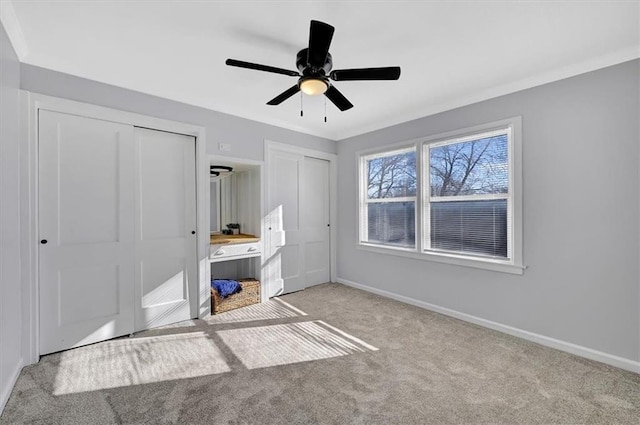 unfurnished bedroom with ceiling fan, baseboards, multiple closets, ornamental molding, and carpet floors