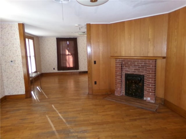 unfurnished living room with wood finished floors, a brick fireplace, and wallpapered walls