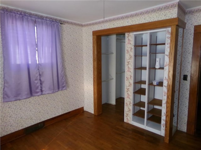 empty room with wood finished floors, crown molding, baseboards, and wallpapered walls