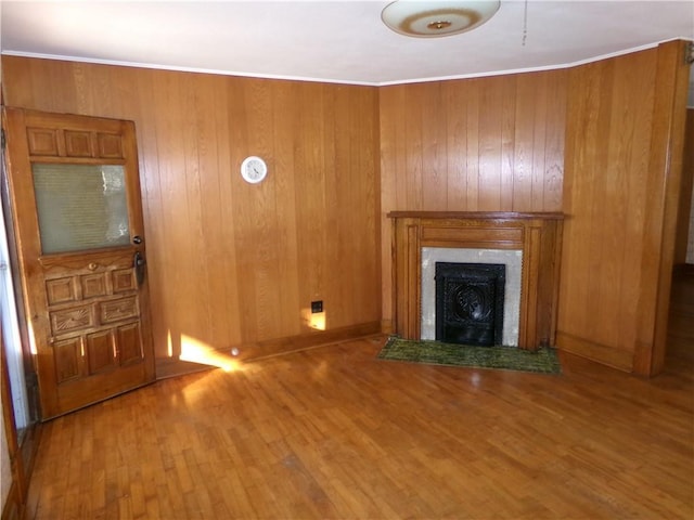 unfurnished living room with ornamental molding, a fireplace, wooden walls, and wood finished floors